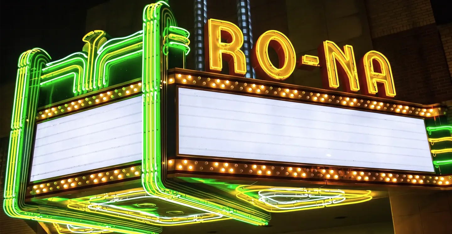 The Ro-Na's restored marquee lit at night — green neon tubes and gold RO-NA lettering above the marquee boards